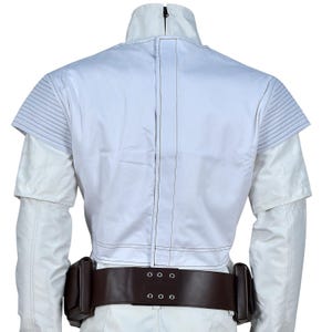 May include: Back view of a white jacket with a high collar and a brown belt with two pouches. The jacket has a zipper and stitched details. The belt has a series of metal eyelets.