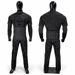 Puede incluir: Traje t&aacute;ctico negro exhibido en un maniqu&iacute;. El traje presenta un cuello alto, paneles reforzados y costuras blancas. El conjunto incluye una chaqueta, pantalones y un cintur&oacute;n. El maniqu&iacute; es negro y el fondo es blanco.