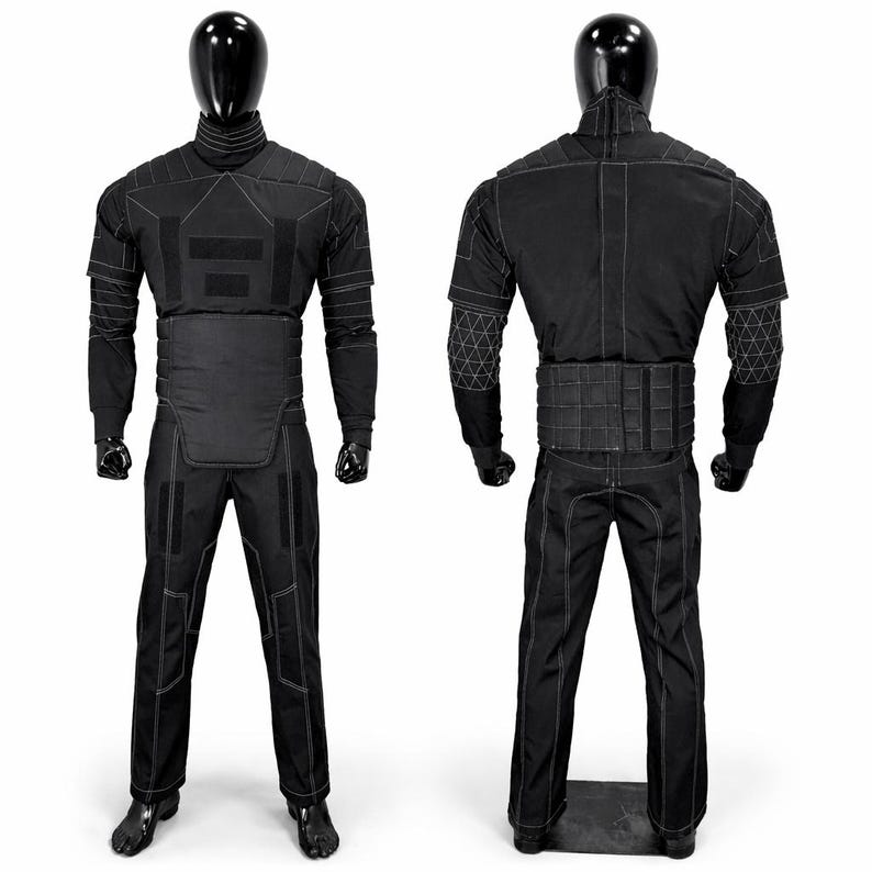 Puede incluir: Traje t&aacute;ctico negro exhibido en un maniqu&iacute;. El traje presenta un cuello alto, paneles reforzados y costuras blancas. El conjunto incluye una chaqueta, pantalones y un cintur&oacute;n. El maniqu&iacute; es negro y el fondo es blanco.