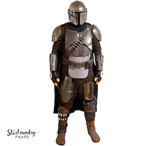 Puede incluir: Un disfraz de cuerpo completo que se asemeja a la armadura mandaloriana. El disfraz presenta un casco plateado, una armadura pectoral y hombreras. El atuendo incluye un traje interior marr&oacute;n oscuro, una capa negra y botas marrones. Incluye el texto "StarFoundry Props".