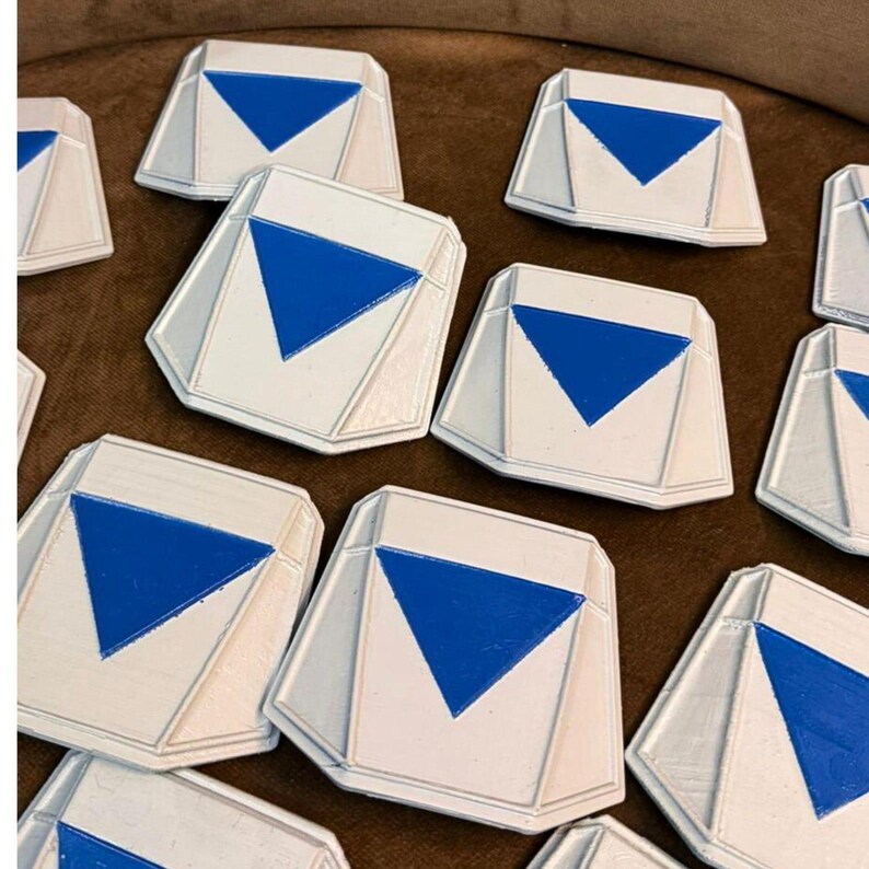 May include: A collection of white, geometric-shaped objects with a blue triangle design. The objects have a raised border and are arranged on a brown surface. The objects appear to be made of a solid material.