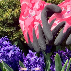 May include: Pink camouflage gardening gloves with black fingertips and the text "LOVE GLOVES" and a pink ribbon. The gloves are set against a backdrop of purple hyacinth flowers and green foliage.