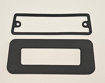 May include: Two black rectangular rubber gaskets. The top gasket has a rectangular cutout and two circular holes. The bottom gasket is larger, also with a rectangular cutout. Both gaskets are on a white background.