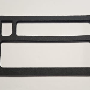 May include: A rectangular black foam insert featuring a textured surface with three distinct cutouts. The layout includes one small square opening on the top left, a long horizontal rectangular opening on the top right, and a large rectangular opening.