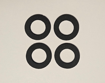 May include: Four black, circular rubber washers arranged in a square pattern. Each washer has a hole in the center. The washers are made of a textured material and are set against a neutral background.