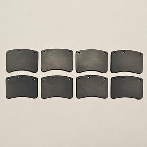 May include: Eight dark gray, curved rectangular objects with three small holes at the top. The objects are arranged in two rows of four against a light background. The objects appear to be made of a solid material.