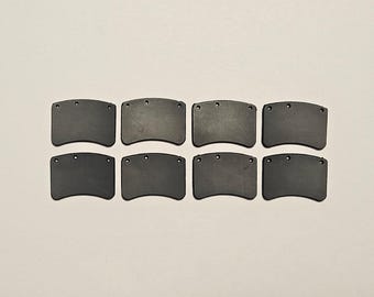 May include: Eight dark gray, curved rectangular objects with three small holes at the top. The objects are arranged in two rows of four against a light background. The objects appear to be made of a solid material.
