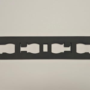 May include: A black, rectangular foam insert with rounded corners. It features four bottle-shaped cutouts and two square cutouts. The insert is designed to hold items securely. The overall design is simple and functional.