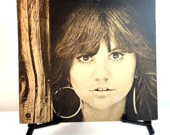Könnte beinhalten: Ein Vintage-Albumcover von Linda Ronstadt mit einem Sepia-Ton-Porträt der Sängerin mit großen Creolen. Das Album wird auf einer schwarzen Staffelei präsentiert. Der Albumtitel ist in goldener Schrift gedruckt.