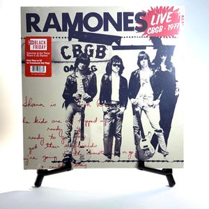 May include: A vinyl record album cover for the Ramones' live album, "CBGB 1977." The cover features a black and white image of the band members. The album title and venue are in bold text. A red sticker indicates it's a Black Friday release.