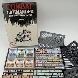 May include: A board game box set titled "Combat Commander 20th Anniversary Edition" with game pieces and cards. The box features a forest silhouette and two soldiers. The game pieces are organised in trays, with various colours and designs.