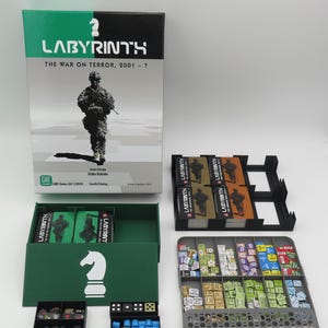 May include: A board game titled "Labyrinth: The War on Terror, 2001 - ?" with a box featuring a soldier graphic. The game includes cards, game pieces, and storage trays. The box is green, black, and white.