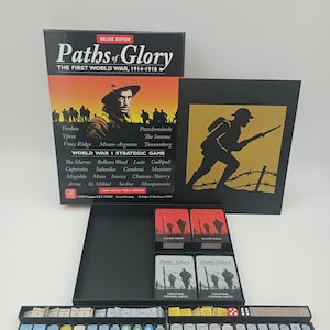 Puede incluir: Edición Deluxe del juego de mesa "Paths of Glory". La caja negra muestra el título del juego y una ilustración de un soldado. Incluye piezas, cartas y dados. Un juego de estrategia sobre la Primera Guerra Mundial.