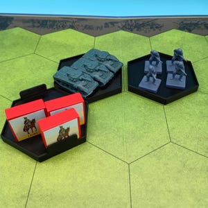 May include: A tabletop war game setup with miniature tanks, soldiers, and card boxes. The tanks and soldiers are gray, and the card boxes are red with a cavalry illustration. The game board is green with hexagonal spaces.