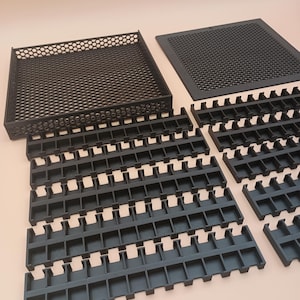 May include: Black plastic organizational trays and inserts. The image shows a rectangular tray with a honeycomb pattern, a flat square piece with a similar pattern, and several rows of slotted inserts. The items are designed for organizing small items.