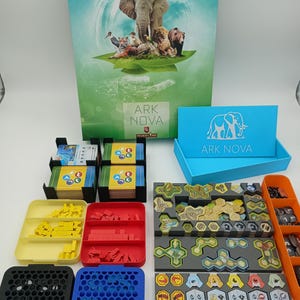 May include: The board game "Ark Nova" is displayed, showing its box with an elephant and other animals. The game includes cards, tokens, and trays in various colours, such as blue, yellow, red, and orange.