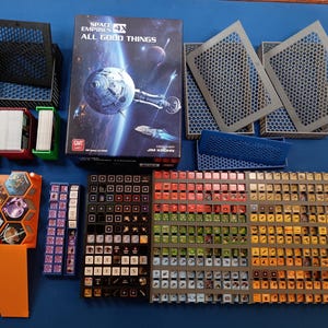 K&ouml;nnte beinhalten: Ein Brettspiel-Setup mit der Box "Space Empires 4X All Good Things". Das Bild zeigt Spielsteine, Kartenhalter und Spielbretter auf einer blauen Oberfl&auml;che. Die Spielkomponenten sind in verschiedenen Farben gehalten.