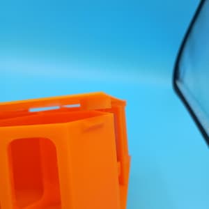 K&ouml;nnte beinhalten: Nahaufnahme eines orangefarbenen Kunststoffbeh&auml;lters mit rechteckiger &Ouml;ffnung und blauem Hintergrund. Der Beh&auml;lter hat ein einfaches, geometrisches Design mit klaren Linien. Der Beh&auml;lter besteht aus einem festen, undurchsichtigen Material.