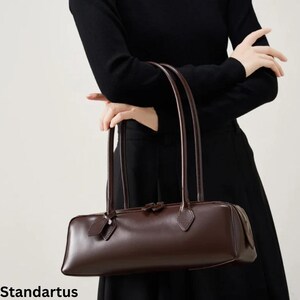 May include: A dark brown rectangular handbag with long, thin handles. The bag has a sleek, minimalist design with a subtle sheen. The word "Standartus" is printed at the bottom of the image.