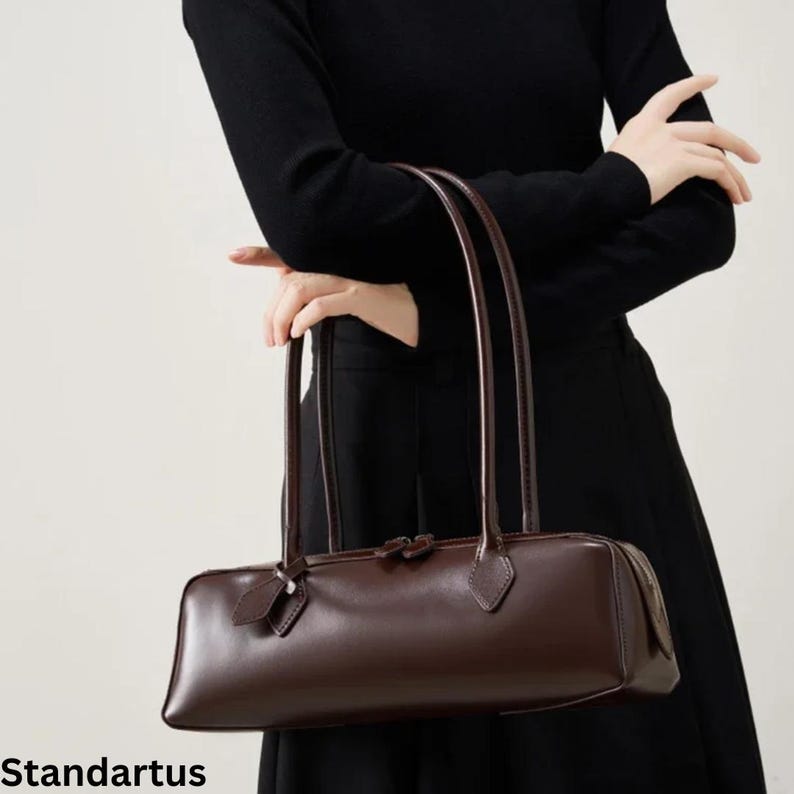 May include: A dark brown rectangular handbag with long, thin handles. The bag has a sleek, minimalist design with a subtle sheen. The word "Standartus" is printed at the bottom of the image.