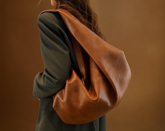 May include: A large, brown leather shoulder bag with a curved design. The bag has a zipper closure and a long strap. The bag is worn over the shoulder. The text "VetroX Leather" is visible at the bottom left.