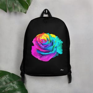 Puede incluir: Mochila negra con un diseño de rosa multicolor. La rosa presenta una gama de colores vibrantes: rosa, amarillo, azul y verde. La mochila tiene un asa superior y correas ajustables.