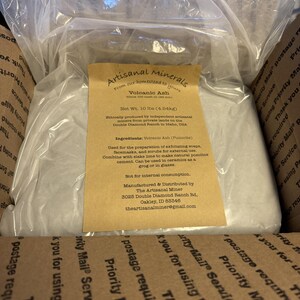 May include: A clear plastic bag containing 10 lbs of volcanic ash, labeled Artisanal Minerals from Double Diamond Ranch in Idaho. The tan paper label lists ingredients as volcanic ash, usage instructions, and contact information for The Artisanal Miner.