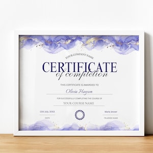 Op de afbeelding: Een ingelijst certificaat van voltooiing met een witte rand. Het certificaat heeft een aquarelontwerp in paarse en gouden tinten aan de boven- en onderkant. De tekst luidt "CERTIFICATE of completion" en bevat ruimte voor een naam, cursus en datum.