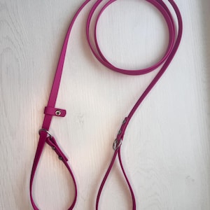 May include: A magenta-colored dog leash with a loop handle and a smaller loop at the end. The leash has a metal ring and a buckle for adjusting the length. The leash is made of a smooth, flexible material.