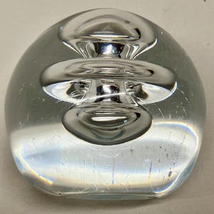 Puede incluir: Un pisapapeles de vidrio transparente con un diseño esférico multicapa de color plateado en el interior.