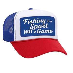 May include: A trucker hat with a red brim, white front panel, and blue mesh back. The front features a blue rectangle with the text "Fishing is a Sport NOT a Game" in white lettering. A red rope trim accents the brim.