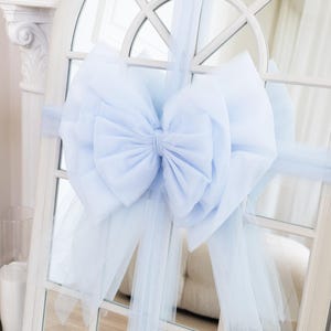 Peut inclure: Un grand nœud bleu clair en tissu superposé et tulle est fixé à un cadre de fenêtre blanc. Le nœud est le point central, avec de longs rubans de tulle flottants qui s'étendent. La fenêtre a un dessus arqué décoratif.