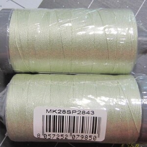 May include: Two spools of pale green thread, wrapped in clear plastic. The spools have gray end caps and are stacked on top of each other. A white label with black barcode and text is visible on the bottom spool.