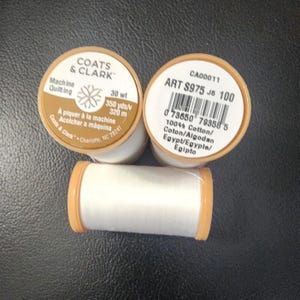 May include: Three spools of white Coats & Clark machine quilting thread. The spools have tan-colored tops and bottoms. The labels include text such as "30 wt" and "350 yds/320 m".
