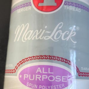 May include: White Maxi-Lock all-purpose spun polyester serger thread spool. The label features a red circle with a sewing machine graphic, the brand name, and the text "All Purpose Spun Polyester".