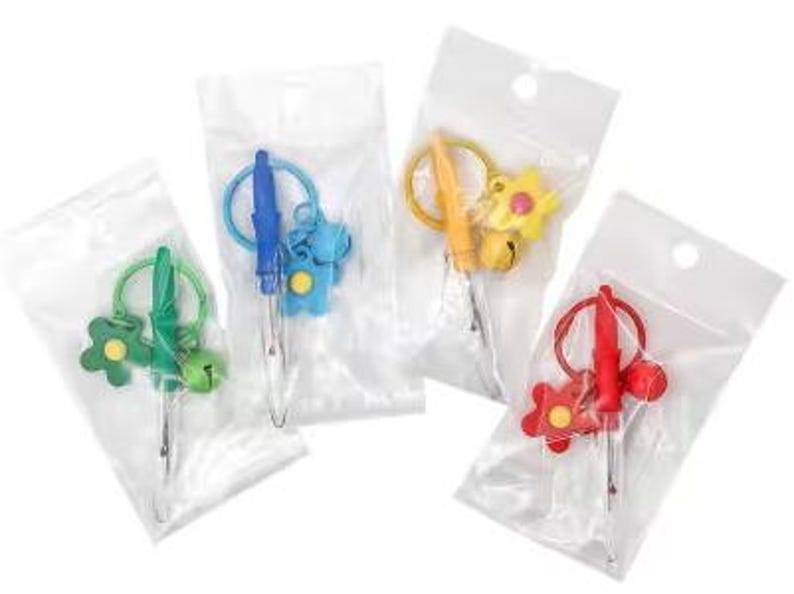 May include: Four colorful yarn needle sets, each packaged in a clear plastic bag. The sets feature different colored handles and decorative charms, including flowers, bells, and a bear. The needles are designed for crafting and sewing projects.