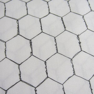 May include: A close-up of a black wire mesh with a hexagonal pattern. The mesh is laid flat on a white surface.