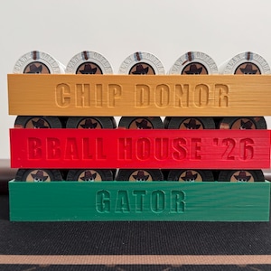 Può includere: Un porta fiches da poker a tre livelli in arancione, rosso e verde. Ogni livello contiene fiches con un disegno di cappello da cowboy. Il livello superiore recita "CHIP DONOR", il centrale "BBALL HOUSE '26" e il inferiore "GATOR".
