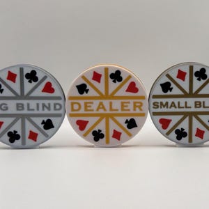 May include: Three poker chips with suit symbols and text. The chips are white, gold, and gray, with red, black, and gold accents. The chips read "BIG BLIND", "DEALER", and "SMALL BLIND".