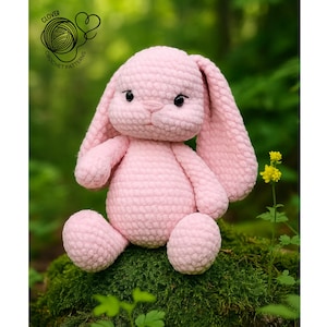 Puede incluir: Un conejo rosa hecho a mano con orejas largas y caídas, sentado sobre una superficie musgosa. El conejo tiene ojos negros y una nariz rosa. La imagen incluye el texto "Clover Crochet Patterns" en un logotipo circular.
