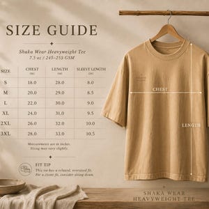 May include: A tan short-sleeve t-shirt hanging on a wooden hanger. A size guide chart is displayed to the left, listing chest, length, and sleeve measurements in inches for sizes S through 3XL. The text Shaka Wear Heavyweight Tee is visible.