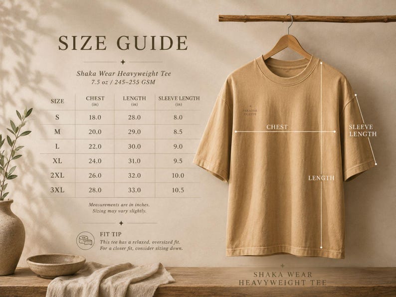 May include: A tan short-sleeve t-shirt hanging on a wooden hanger. A size guide chart is displayed to the left, listing chest, length, and sleeve measurements in inches for sizes S through 3XL. The text Shaka Wear Heavyweight Tee is visible.