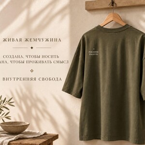 以下が含まれることがあります： 木製ハンガーに掛けられたオリーブグリーンの半袖Tシャツ。シャツの背面、襟元付近には「PARADISE PALETTE」という小さな白い文字がプリントされています。クルーネックで、ドロップショルダーのゆったりとしたシルエットが特徴です。
