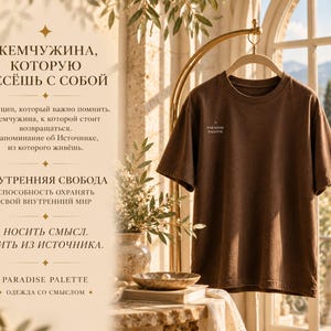 以下が含まれることがあります： クルーネックの無地の茶色の半袖Tシャツで、左胸に小さな白い文字で「PARADISE PALETTE」とプリントされています。Tシャツはハンガーに掛けられており、背景にはロシア語のテキストが書かれた明るい色の壁があります。