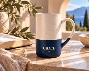 Peut inclure: Une grande tasse en céramique cylindrique présentant un design bicolore avec une partie supérieure crème mouchetée et une partie inférieure bleu marine unie. Le mot GRACE est imprimé en lettres capitales blanches au-dessus d'une étoile.