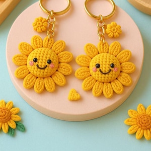 Può includere: Due portachiavi a forma di girasole giallo all'uncinetto con anelli color oro. Ogni girasole ha una faccia sorridente con guance rosa. Un piccolo ciondolo a forma di fiore giallo pende dalla catena. I portachiavi sono su un cerchio rosa.