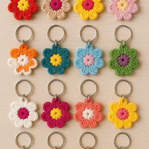 May include: A collection of sixteen crochet flower keychains in various colors, including red, yellow, pink, orange, green, blue, and white. Each flower has a contrasting center and a silver-colored metal keyring.