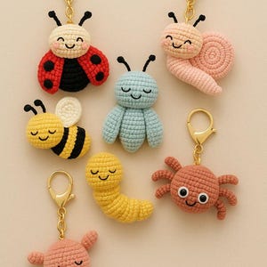 Può includere: Una collezione di portachiavi all'uncinetto fatti a mano con vari disegni di insetti sorridenti. Include una coccinella, una lumaca, un'ape, un insetto blu, un verme, un ragno e una creatura rosa, tutti con portachiavi dorati.