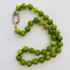 Puede incluir: Un collar con grandes cuentas redondas de color verde lima ensartadas en un cordón azul. El collar se asegura con un cierre plateado. Las cuentas tienen un acabado pulido y varían ligeramente en tono. El collar se muestra sobre un fondo blanco.