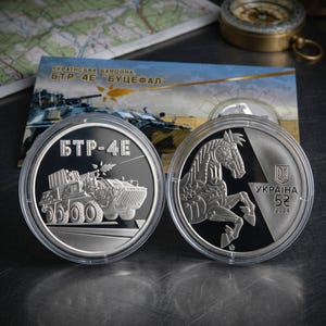 May include: Two circular silver-toned commemorative coins in protective cases. One coin features a BTR-4E armored vehicle with the text BTR-4E. The other coin displays a stylized horse, the text UKRAINA, the number 5, and the year 2024.